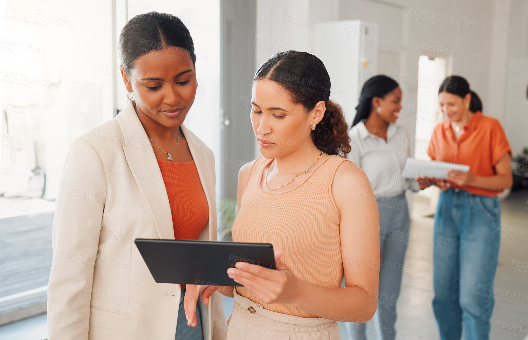 Buy stock photo Two mixed race businesswomen talking and working on a digital tablet  together at work. Hispanic businesspeople talking and planning while looking at a digital tablet in an office