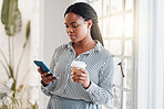 Young african american businesswoman using her phone while drinking a coffee alone in an office at work. One black woman using social media on her cellphone and holding a coffee cup on a break standing at work