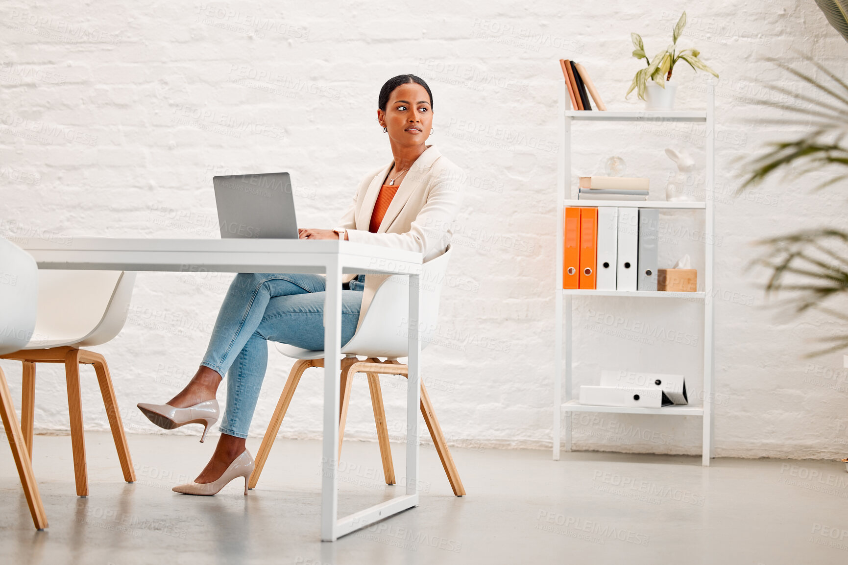Buy stock photo Young mixed race businesswoman thinking while working on a laptop at a table in an office at work. One hispanic businessperson typing on a laptop while sitting in a chair at a desk