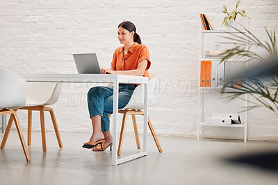 Buy stock photo Young content mixed race businesswoman working on a laptop at a table in an office at work. One hispanic businessperson typing an email on a laptop while sitting in a chair at a desk