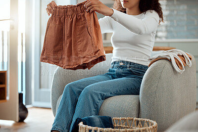 Buy stock photo Woman folding a pair of shorts. Woman relaxing at home cleaning clothing. Woman sitting in a chair folding laundry. Woman doing housework chores at home cropped. Mixed race woman folding neat clothing