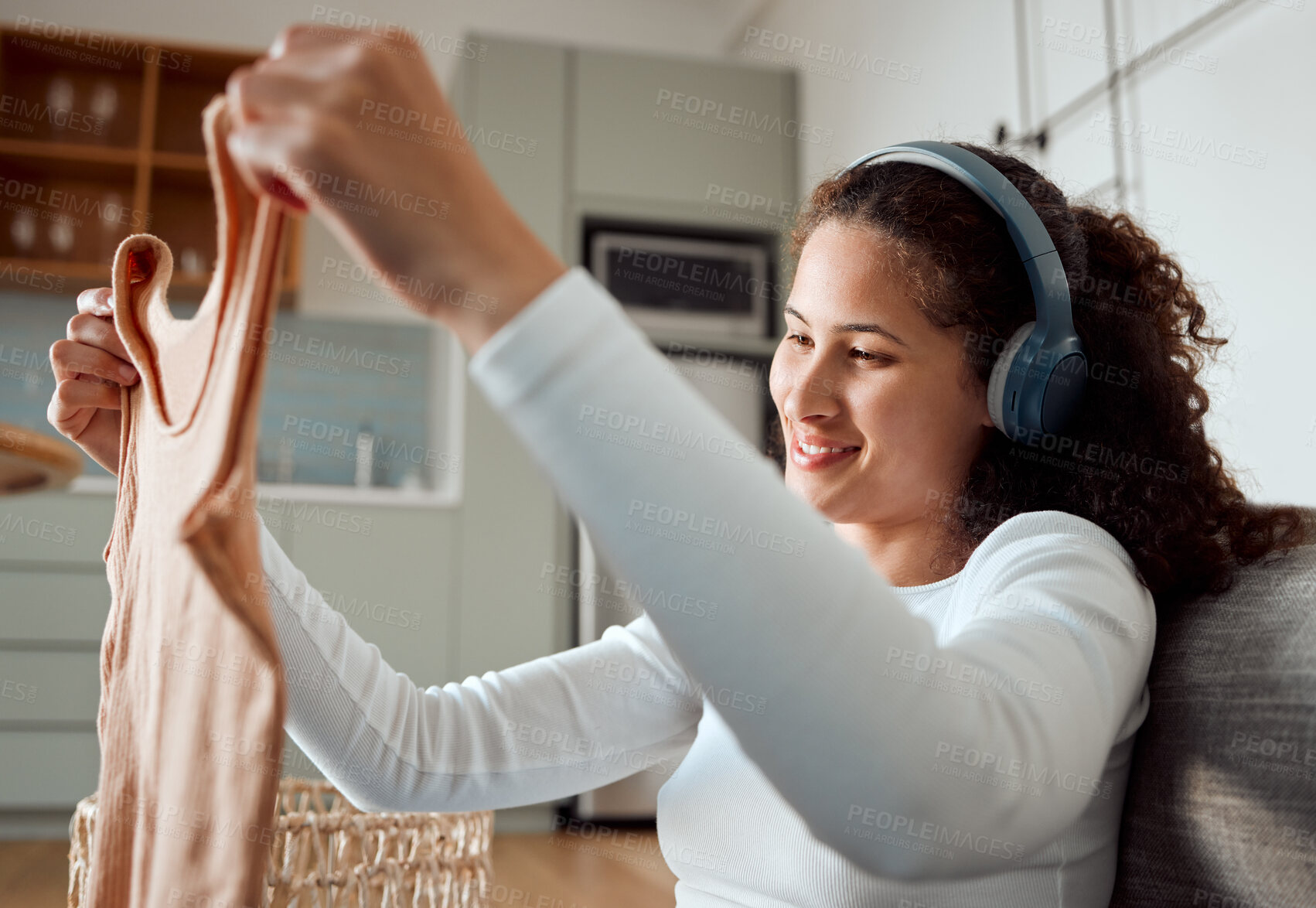 Buy stock photo Young woman enjoying music and housework. Hispanic woman looking at a clean tshirt. Smiling woman enjoying her chore routine. Young woman using headphones for music. Woman folding a washed top
