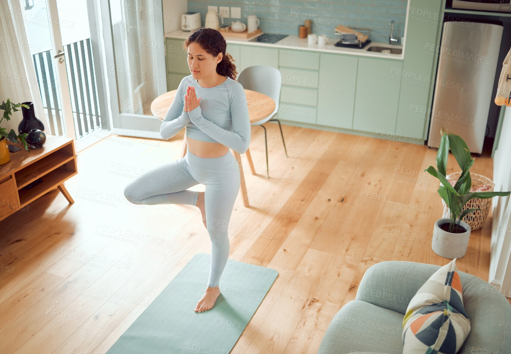 Buy stock photo Beautiful young mixed race woman meditating while standing in an upright position while practicing yoga at home. Hispanic female exercising her body and mind, finding inner peace, balance and clarity