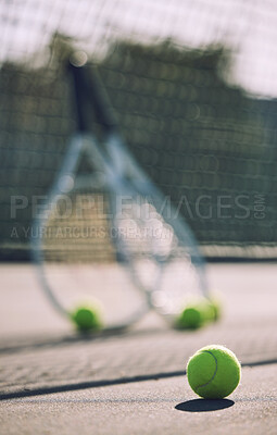 Buy stock photo Group of tennis balls and rackets against a net on an empty court in a sports club during the day. Playing tennis is exercise, promotes health, wellness and fitness. Gear and equipment after a game