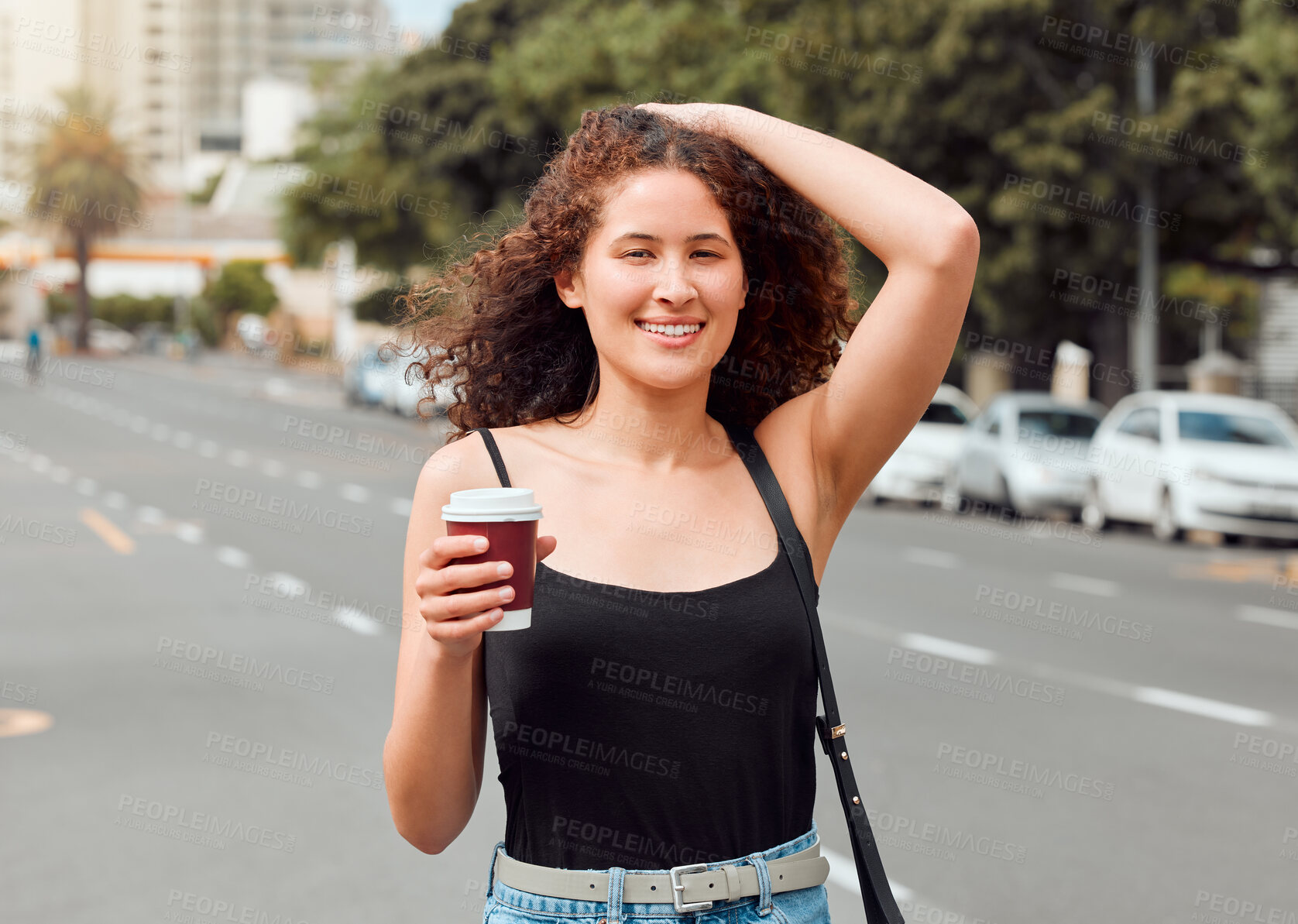 Buy stock photo Portrait of a happy beautiful young mixed race woman exploring the city while holding a takeaway coffee and touching her curly brunette hair. Hispanic tourist enjoying the view downtown on the weekend