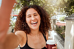 Mixed race young woman taking a selfie while out exploring the city. Portrait of a smiling tourist holding a coffee and taking a photo while enjoying her weekend downtown. 