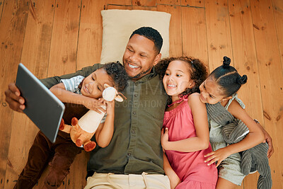A happy mixed race family of four relaxing and lying on the lounge floor together. Loving black single parent bonding with his kids while using a digital tablet to watch movies
