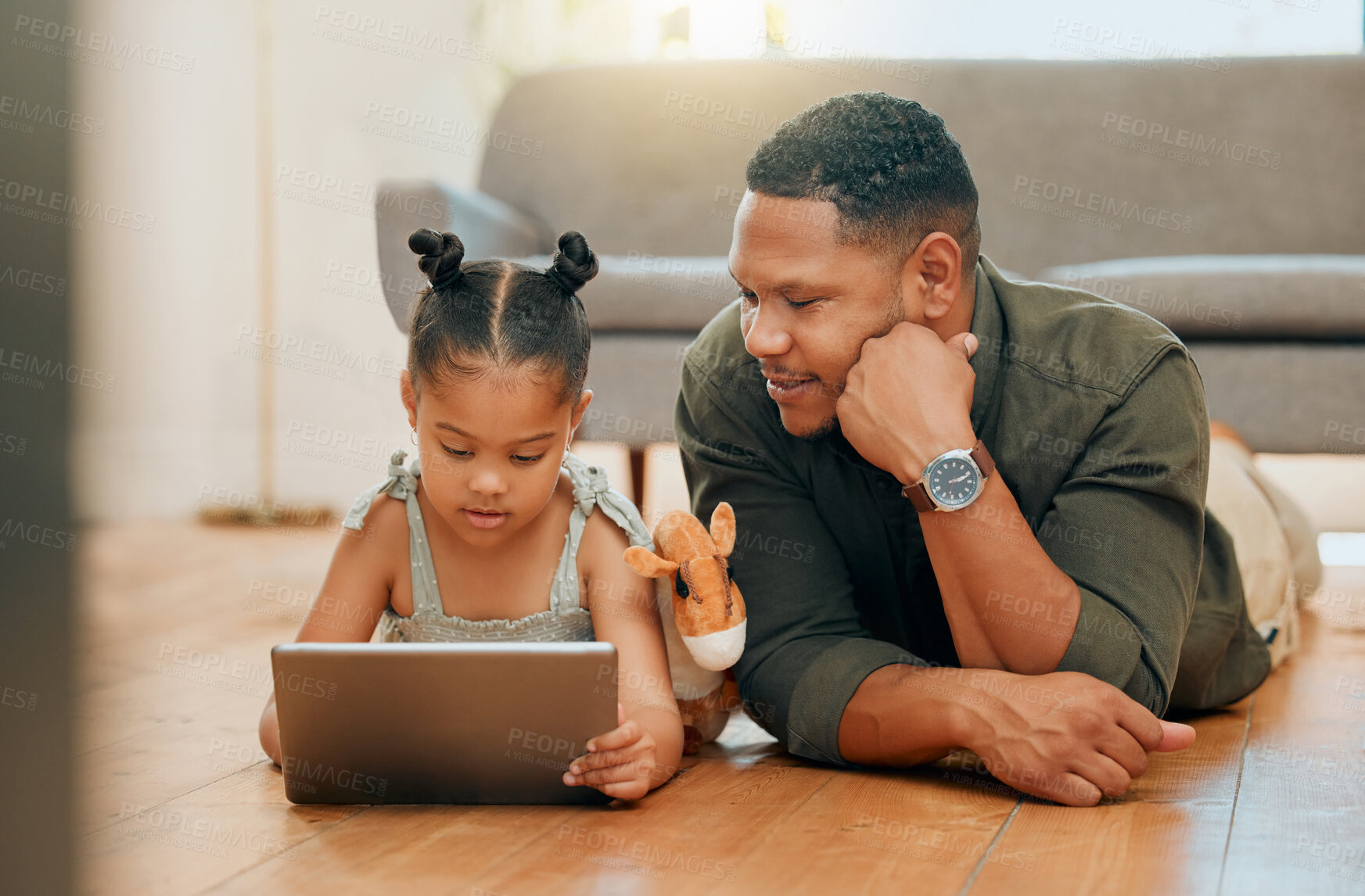 Buy stock photo A happy mixed race family of two relaxing and lying on the lounge floor together. Loving black single parent bonding with his daughter while using a digital tablet to watch movies