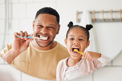 Happy mixed race father and daughter brushing their teeth together in a bathroom at home. Single African American parent teaching his daughter to protect her teeth