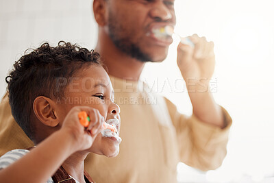 Happy mixed race father and son brushing their teeth together in a bathroom at home. Single African American parent teaching his son to protect his teeth