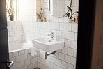A clean and tidy bathroom inside a house. A basin, bath, with ceramic tiling and a round mirror hanging on the wall. A clean, hygienic, bright room