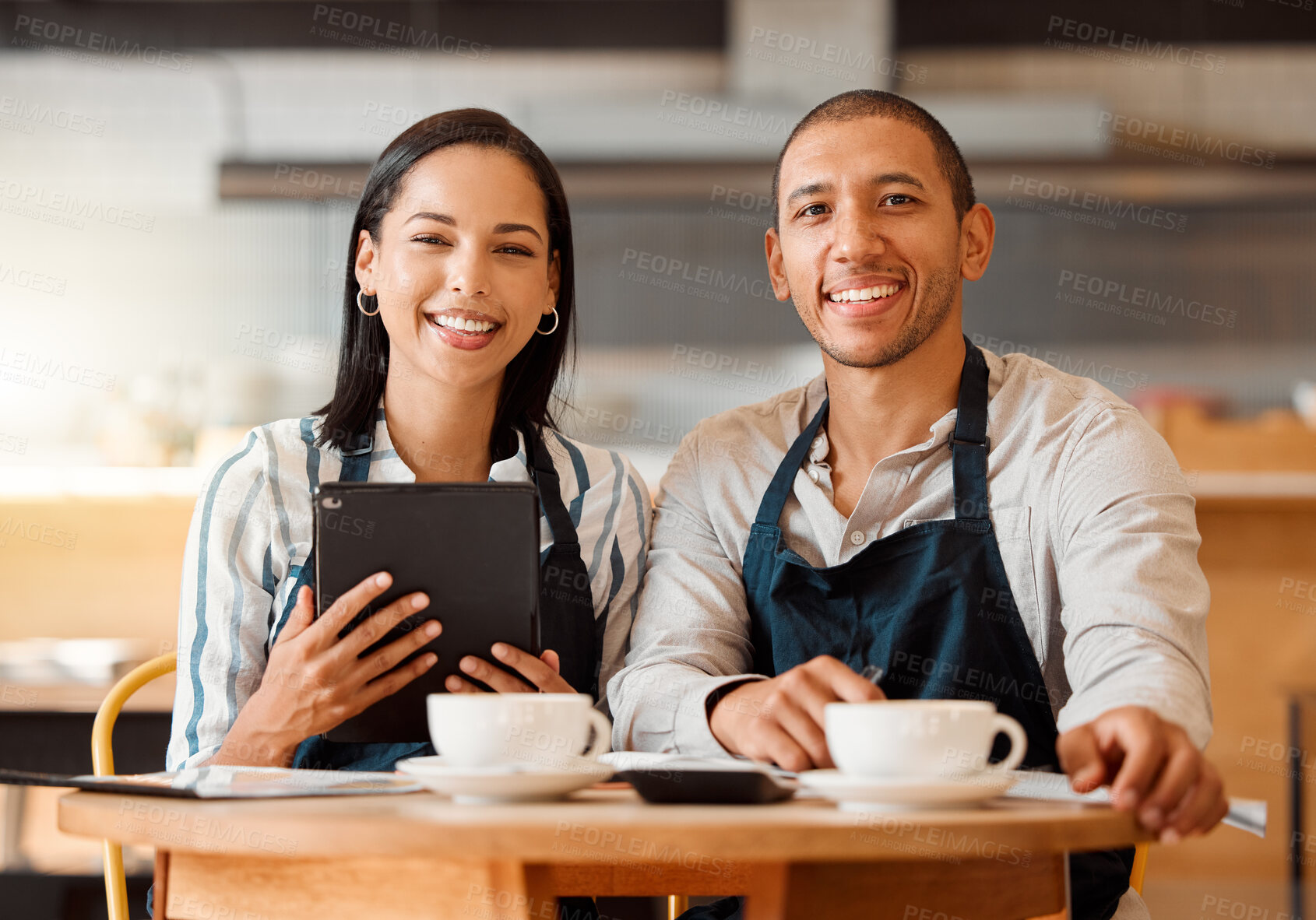 Buy stock photo Two restaurant workers planning on a digital tablet in a small business. Young mixed race colleagues having coffee while reviewing plans in a cafe. Colleagues doing digital stocktake and calculations