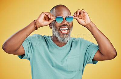 Happy mature African American man standing alone against yellow background in a studio and posing with sunglasses. Smiling black man feeling fashionable and cool while wearing glasses. Summer and beach