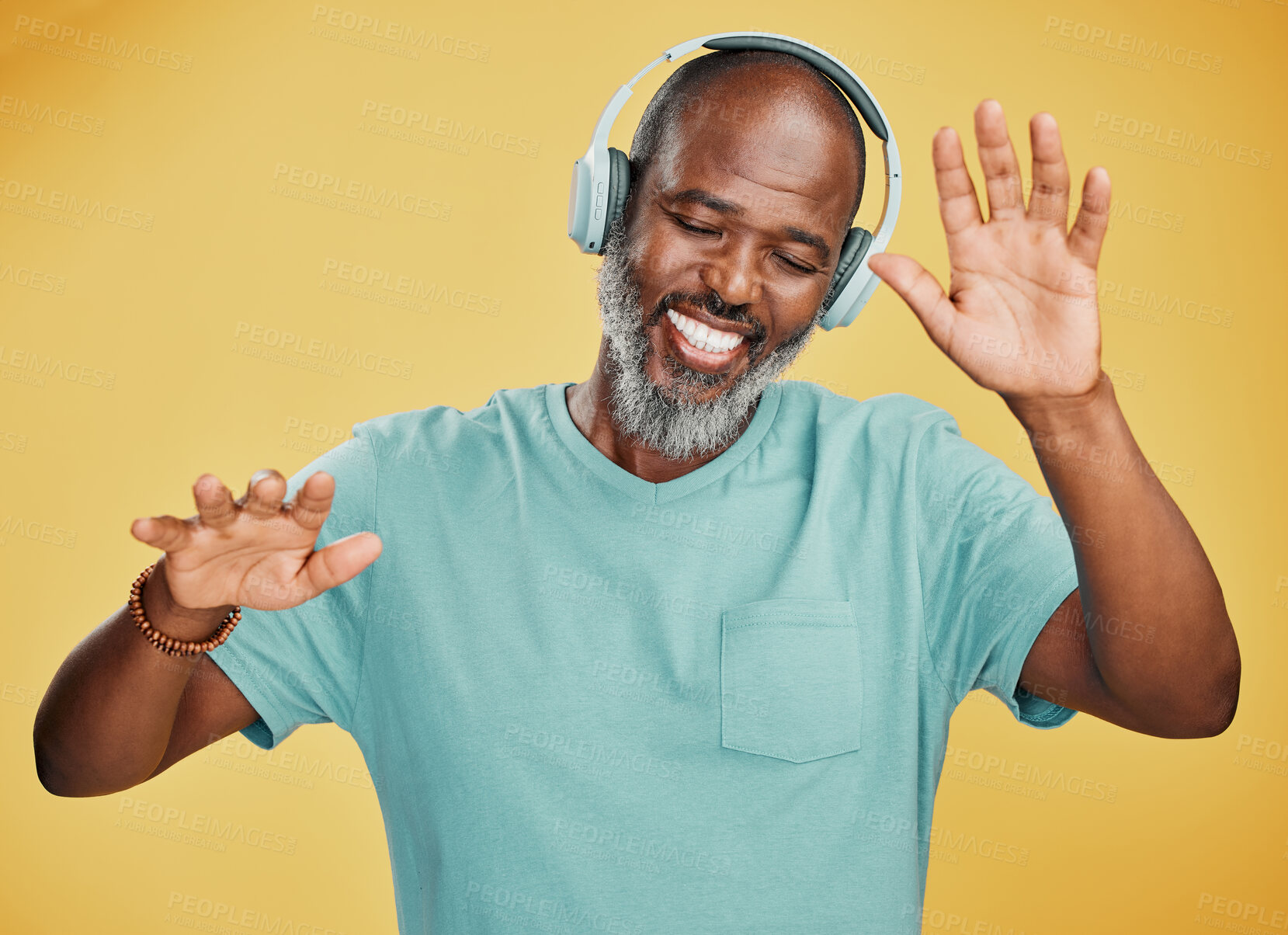 Buy stock photo Happy mature african man dancing while listening to music with headphones against a yellow studio background. Carefree senior black man with grey beard celebrating to and enjoying his favourite songs
