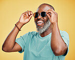 Happy mature African American man standing alone against yellow background in a studio and posing with sunglasses. Smiling black man feeling fashionable and cool while wearing glasses. Summer ready