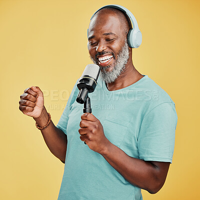 Buy stock photo Happy mature African American man against a yellow studio background wearing headphones to listen to music while singing karaoke with a microphone. Smiling black man enjoying and holding a mic to sing