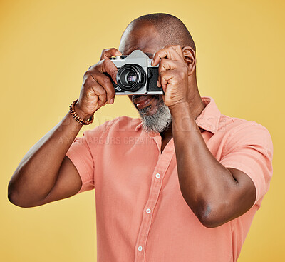 One African American man standing alone against a yellow background in a studio and taking pictures on a camera. Confident black man holding a camera and taking photographs as a hobby. Smile and pose