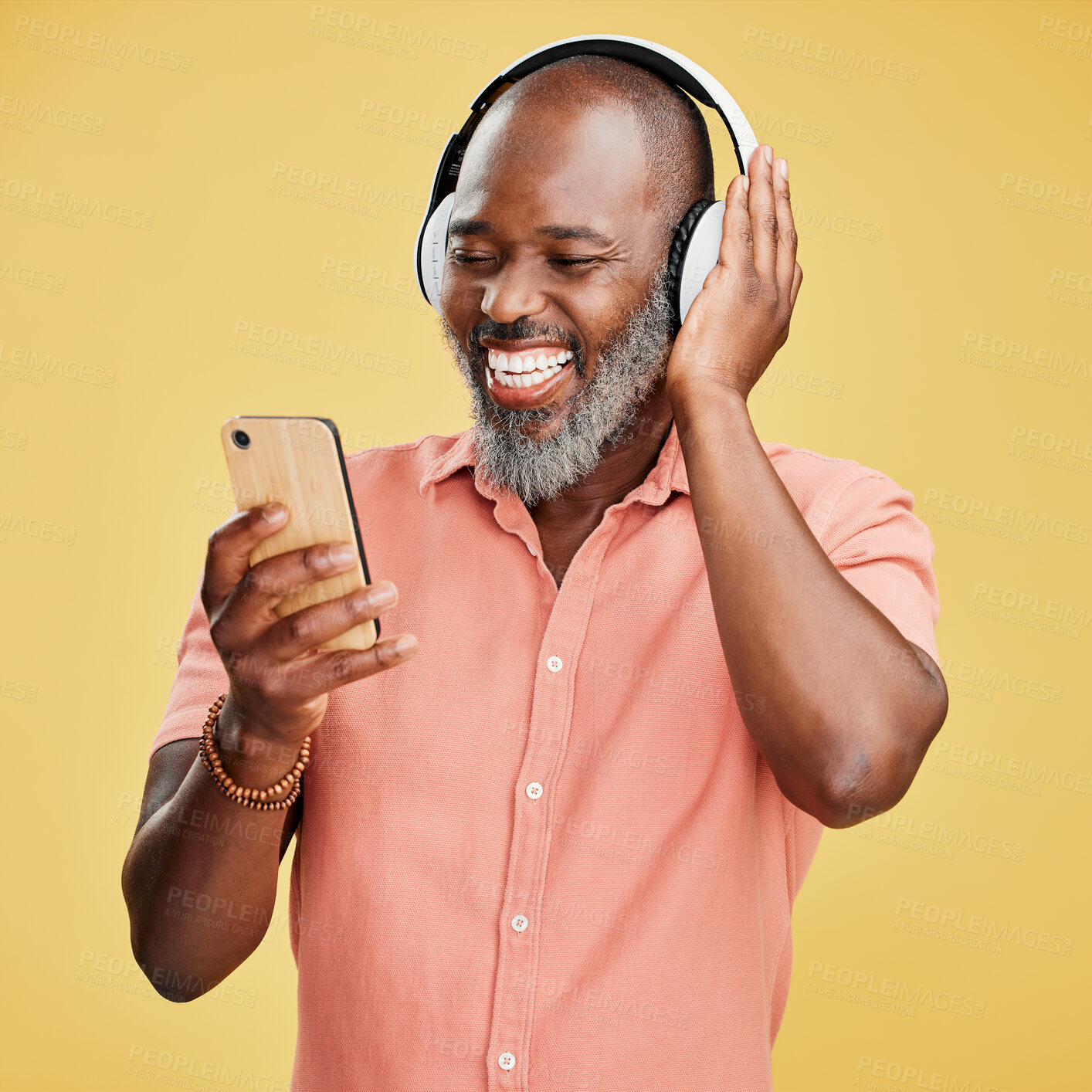 Buy stock photo One mature african american man listening to music using wireless headphones while isolated against a yellow background. Happy man with a grey beard smiling while streaming on his phone in studio