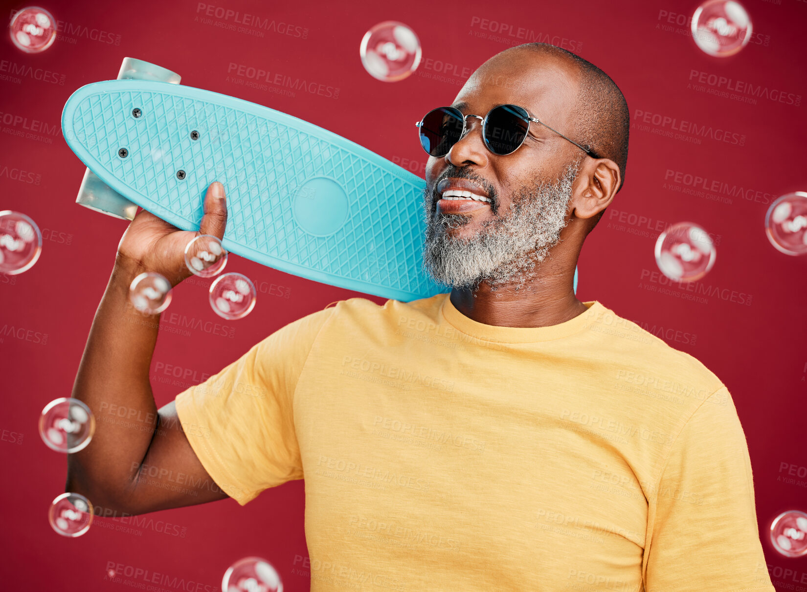 Buy stock photo One mature african american man standing with a skateboard surrounded by bubbles against a red studio background. Happy and carefree black man wearing sunglasses and smiling, ready for summer and fun