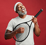 One happy mature african american man standing against a red background in studio waiting for his match to begin. Smiling black man feeling fit and sporty while playing music on his tennis racquet