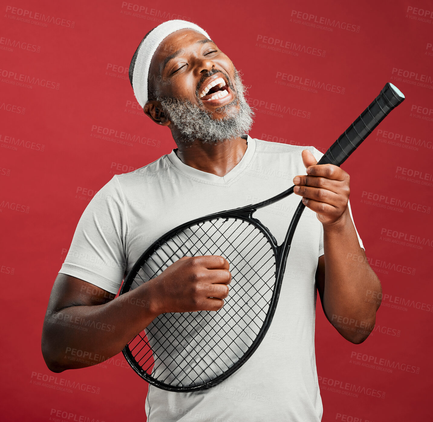 Buy stock photo A mature african american male using a tennis racket as a guitar and singing against a red studio background. Black african man wearing a sweatband on his head having fun and smiling while singing. You've got to let your voice be heard