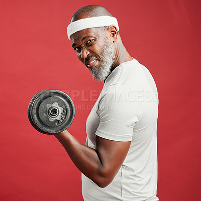Confident mature african american man standing alone against a red background in a studio and posing with dumbbells. Focused black man feeling sporty and fit while working out. A heathy lifestyle