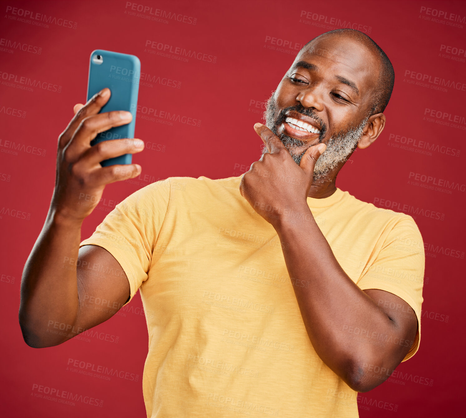 Buy stock photo One contemplative trendy mature african american man taking a selfie on a smart phone against a red studio background. Fashionable black man standing and posing while taking pictures for social media