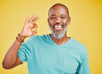 Mature african american man looking happy and smiling while making an okay gesture with his hand against a yellow studio background. Expressing that everything is perfect. Showing support