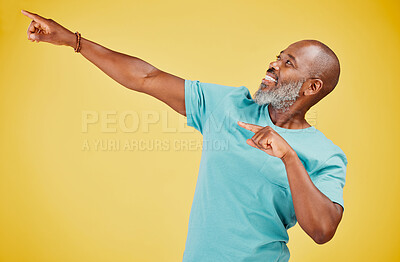 Mature african man smiling and pointing in a direction against a yellow studio background. Black guy looking happy and making a pointing gesture reacting with a smile while looking cheerful and happy. Stay positive you never know what\'s coming next