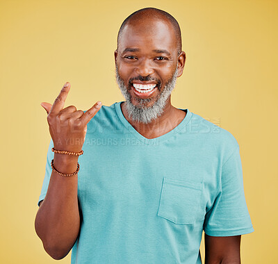 Portrait of a mature friendly african american man looking happy and smiling while making an rock on hand gesture against a yellow studio background. Expressing that you need to To party to rock music. An expression of celebration