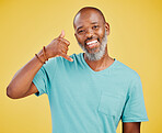 Portrait of a mature african american male making a phone hand gesture while smiling against a yellow studio background. Black african man looking happy and signaling a phone with his hand. Just one phone call away