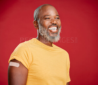 Buy stock photo Mature african american man with a beard smiling and looking happy while wearing a bandaid on his arm and standing against a red studio background. Vaccination, health and healthcare