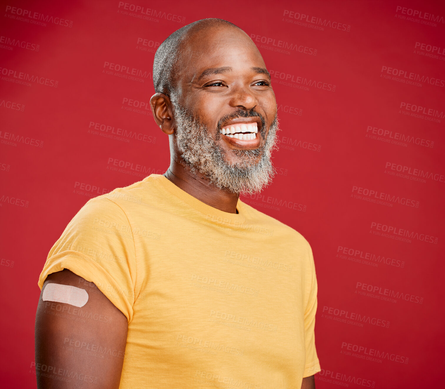 Buy stock photo Mature african american man with a beard smiling and looking happy while wearing a bandaid on his arm and standing against a red studio background. Vaccination, health and healthcare