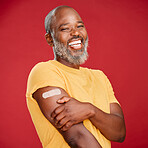 Mature african american man with a beard smiling and looking happy while wearing a bandaid and holding his arm and standing against a red studio background. Vaccination, health and healthcare