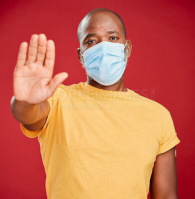 Portrait of a mature black man wearing a mask to stop the spread of corona and making a stop hand gesture against a red studio background. African american man wanting distance to covid. Social distancing should not be taken lightly