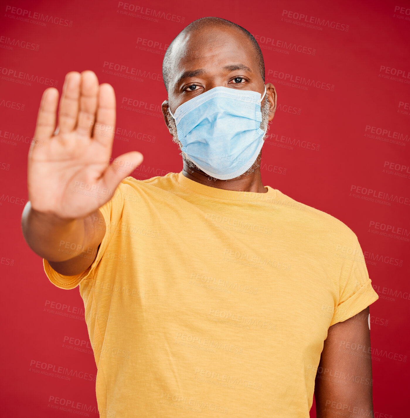 Buy stock photo Portrait of a mature black man wearing a mask to stop the spread of corona and making a stop hand gesture against a red studio background. African american man wanting distance to covid. Social distancing should not be taken lightly 