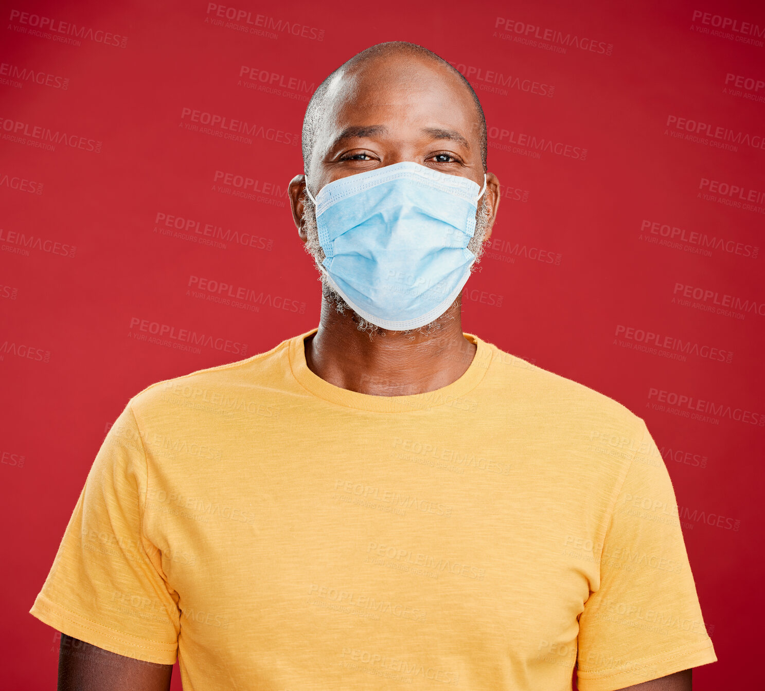 Buy stock photo A african american making wearing mask to stop the spread of coronavirus and standing against a red studio background. Black male looking positive while wearing a mask. Let's stop the spread of covid and look after our health