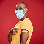 Portrait of a african american making wearing mask to stop the spread of coronavirus and standing against a red studio background. Black african male wearing a mask and making a pointing gesture with his hand. Getting vaccinated is the key to the victory 