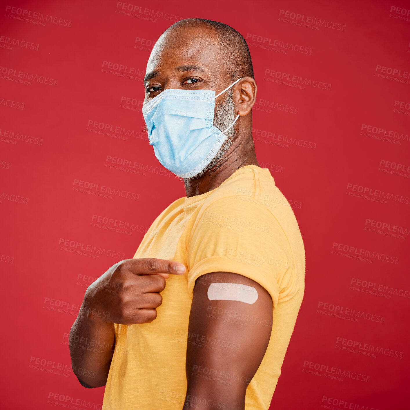 Buy stock photo African man, covid and vaccine in studio portrait with pride, healthcare and wellness by red background. Black male model, face mask and point at arm with plaster, medicine and safety to stop virus