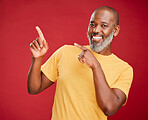 Mature african man smiling and pointing in a direction against a red studio background. Black guy looking happy and making a pointing gesture reacting with a smile while looking cheerful and happy. Stay positive you never know what's coming next