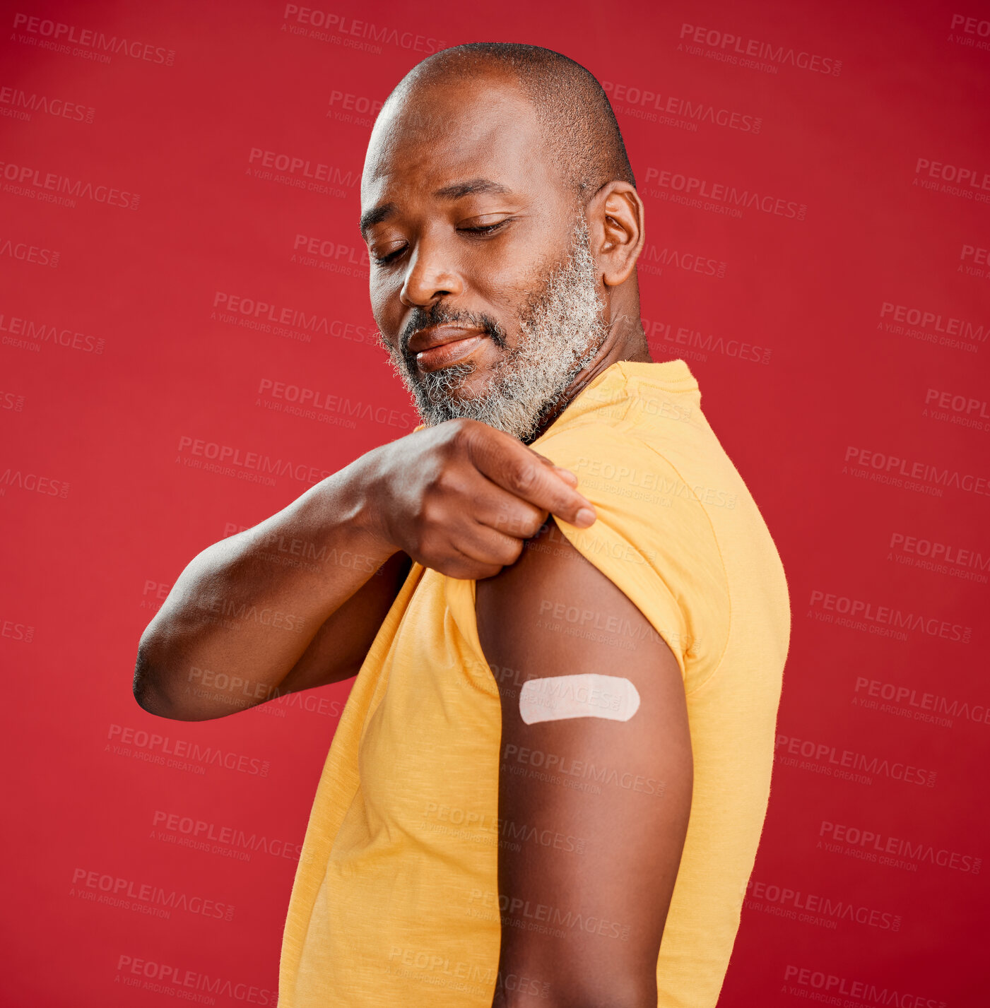 Buy stock photo Mature african american man with a beard smiling and looking happy while wearing a bandaid and standing against a red studio background. Vaccination, health and healthcare is important to cure the virus