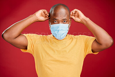 Young african american man wearing a mask standing against a red studio background. Health, healthcare, safety. Sick, disease, risk. covid, outbreak, virus