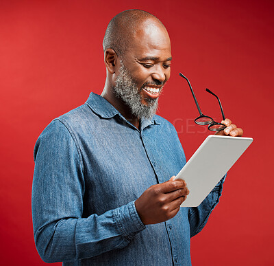 One happy mature african american man isolated against a red background in a studio and browsing the internet on a digital tablet. Smiling black man using glasses to read social media and new trends