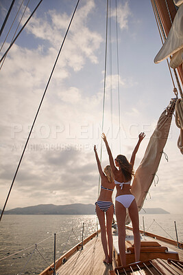Buy stock photo Cheerful friends celebrating on a holiday cruise together. Two women in bikinis celebrating on a boat cruise around Italy. Happy friends on a yacht cruise cheering with arms raised