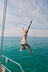 Excited young woman jumping off a boat during a holiday cruise to swim in the ocean. Young woman in bikini ready to swim in the ocean after excitedly jumping from boat