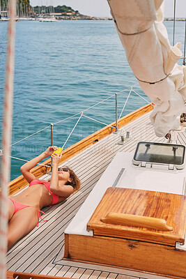 Young woman in a red bikini sunbathing on a boat lying down using her smartphone to send messages. Woman lying on boat using smartphone to scroll apps while sunbathing.