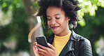 A young woman with afro using her cellphone to read text messages while in a park. A young woman in the park smiling and scrolling through apps on her smartphone. A happy young woman with an afro