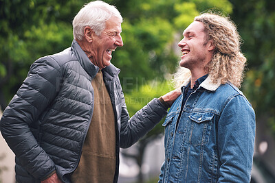 Buy stock photo A mature man talking to his young son and laughing while touching his shoulder. A proud father relaxing with his son in the park laughing and talking. Two family members bonding in the park