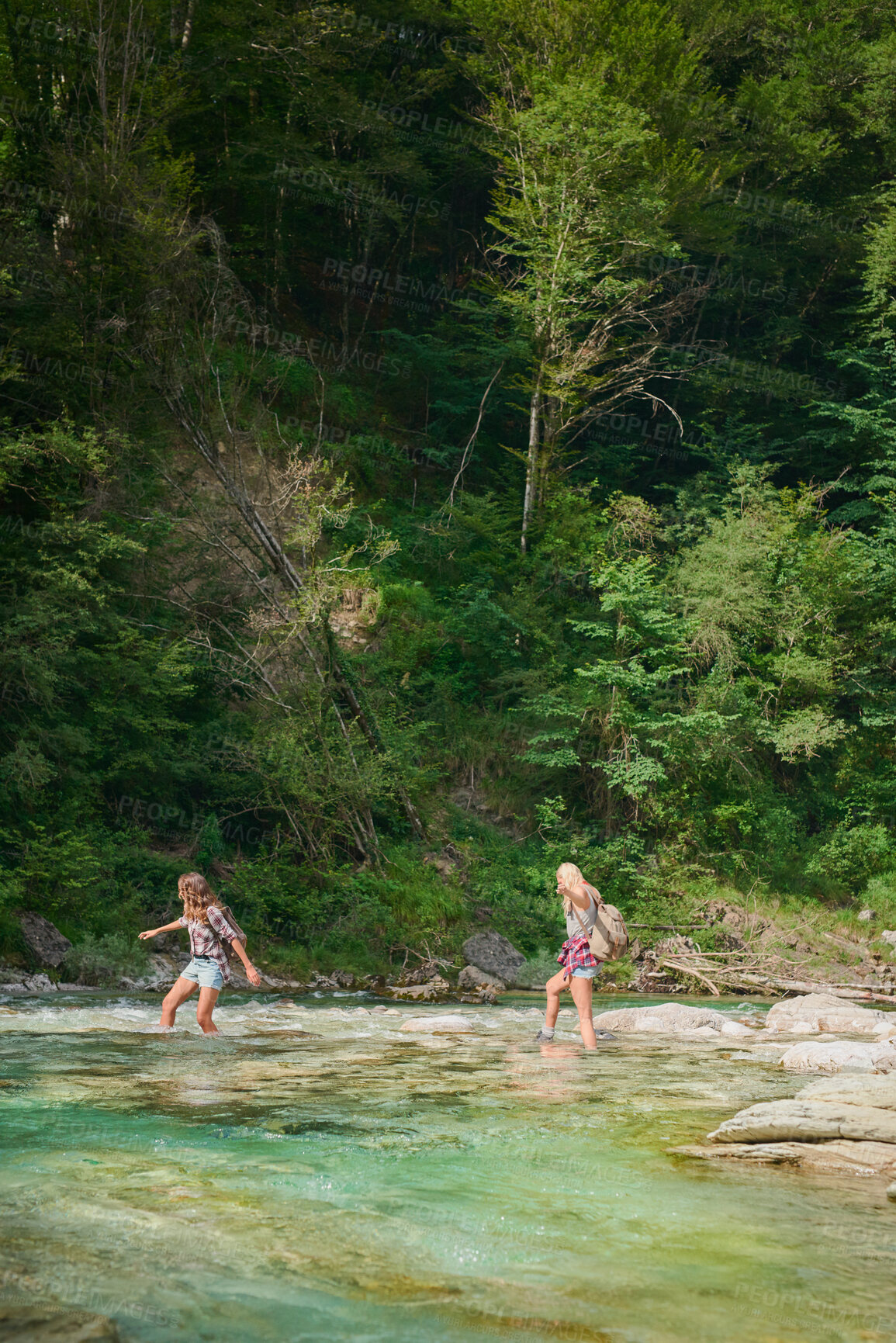 Buy stock photo Two young friends crossing a river on a travel adventure exploring nature together. Carefree women walking across rocks in a lake, having fun on a summer vacation