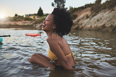 Buy stock photo Cheerful African american woman with afro wearing a bikini while sitting in lake. Carefree woman laughing and having fun while out for a swim in river, lake or beach